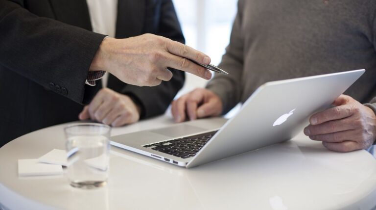 Επιχειρηματίας δείχνει σε συνεργάτη του ένα αρχείο σχετικό με Ψηφιακή κάρτα εργασίας στην οθόνη του laptop