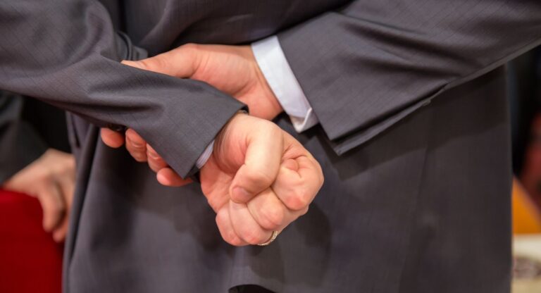 Επιχειρηματίας με τα χέρια σφιγμένα πίσω στη πλάτη προβληματίζεται σχετικά με την Ακυρωσία Αποφάσεων ΓΣ:  Μη Χορήγηση Οφειλόμενων Πληροφοριών (άρ. 141) & Κατάχρηση Εξουσίας Πλειοψηφίας